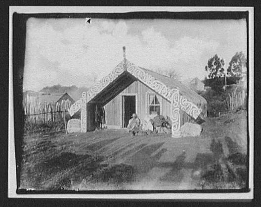 Man, woman and baby in front of ornamented Maori house, New Zealand, 1895