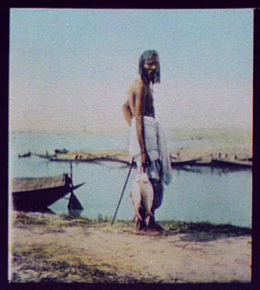 Man holding string of fish; fishing boats in background, India, 1895