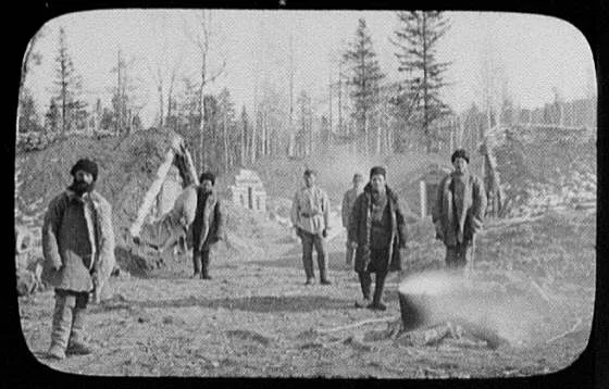 Convicts standing in camp between sod-roofed houses, Russia, 1895
