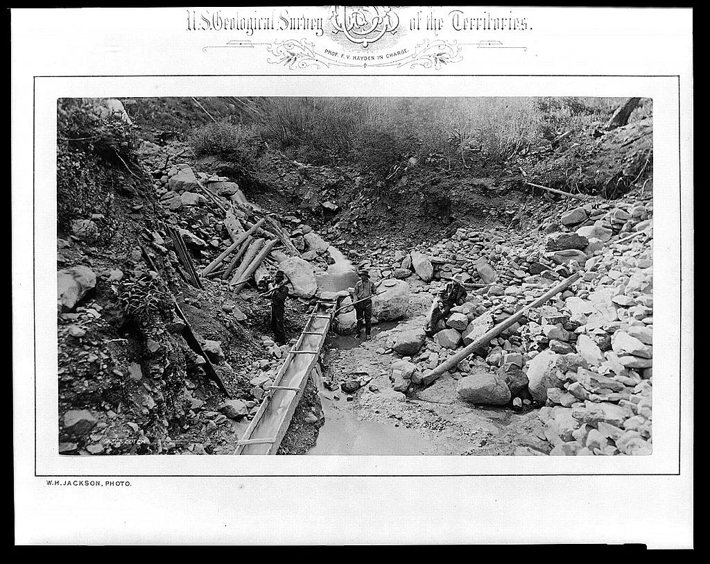 [Three men in gulch with a sluice, placer mining for gold], 1872